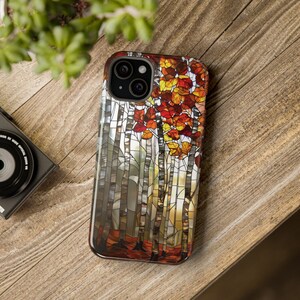 May include: A smartphone case featuring a stained-glass design of birch trees with red, orange, and yellow autumn leaves. The case has a glossy finish and a black camera module.