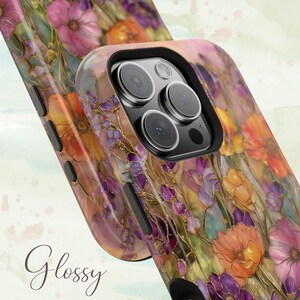 Op de afbeelding: Glanzende telefoonhoes met een levendig bloemenontwerp met roze, oranje en paarse bloemen. De hoes heeft een zwarte camera-uitsparing en het woord "Glossy" in cursief.