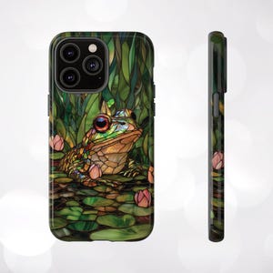 May include: A green, brown, and blue stained glass phone case with a frog sitting on lily pads. The phone case has a cutout for the camera lens.