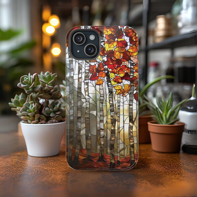 May include: A smartphone case featuring a stained-glass design of birch trees with autumn leaves in shades of red, orange, and yellow. The case has a black border and a camera cutout.