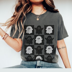 May include: A gray t-shirt with a checkered pattern of white and black ghosts. The shirt has a distressed look.
