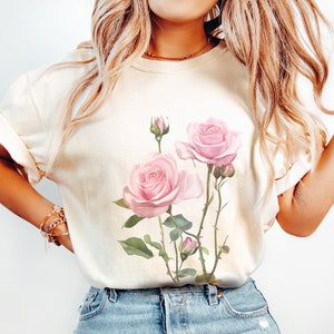May include: A white t-shirt with a pink rose floral print. The roses are pink with green leaves and stems.