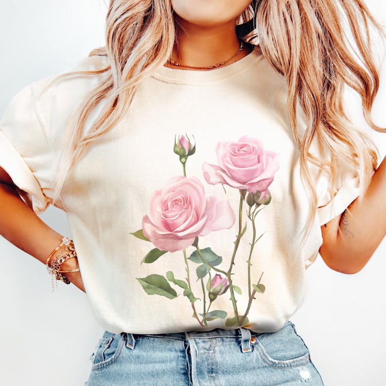 May include: A white t-shirt with a pink rose floral print. The roses are pink with green leaves and stems.
