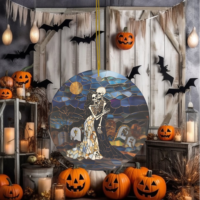 May include: A round, stained glass ornament featuring a skeleton couple embracing in a graveyard setting. The ornament is decorated with a blue, purple, and gold color scheme and features a full moon in the background.
