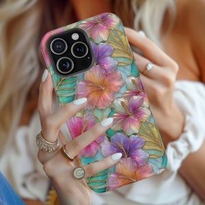May include: A smartphone case featuring a vibrant floral pattern with hibiscus flowers in shades of pink, purple, and orange, accented by green leaves and gold-toned outlines. The design has a stained-glass appearance with a glossy finish.