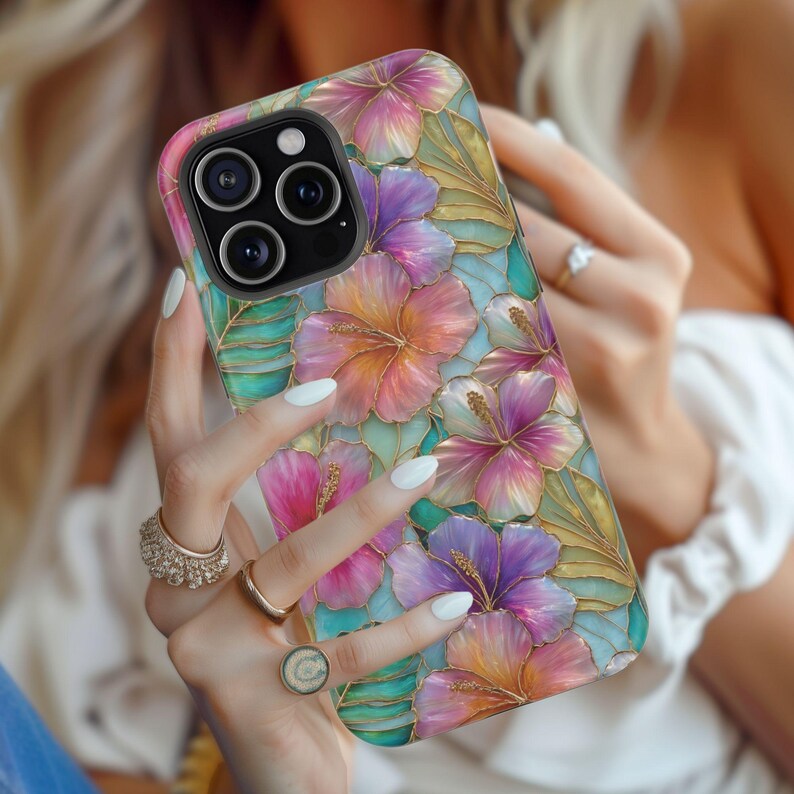 May include: A smartphone case featuring a vibrant floral pattern with hibiscus flowers in shades of pink, purple, and orange, accented by green leaves and gold-toned outlines. The design has a stained-glass appearance with a glossy finish.