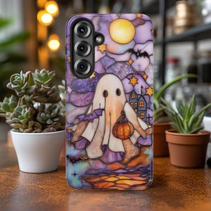 May include: A phone case featuring a stained-glass design with a Halloween theme. The artwork depicts a ghost holding a pumpkin, a full moon, stars, bats, and a haunted house, all in shades of purple, orange, and white.