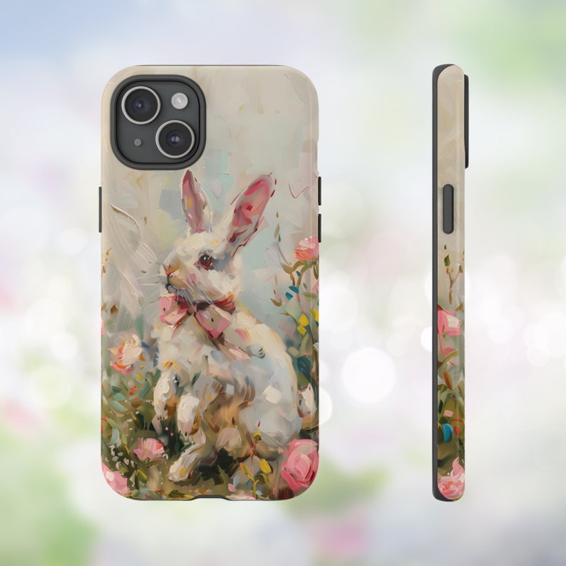 K&ouml;nnte beinhalten: Ein wei&szlig;es Kaninchen mit einer rosa Schleife sitzt in einem Blumenfeld. Das Kaninchen ist in einem realistischen Stil mit weichen, pastellfarbenen Farben gemalt. Der Hintergrund ist hellblau mit einem Hauch von Gr&uuml;n. Die Handyh&uuml;lle ist aus strapazierf&auml;higem Material gefertigt und sch&uuml;tzt Ihr Handy vor Kratzern und St&ouml;&szlig;en.