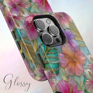May include: A glossy phone case featuring a vibrant floral pattern with pink and orange hibiscus flowers, teal tropical leaves, and gold-toned outlines. The case has a black camera cutout frame and black side buttons for a smartphone device.