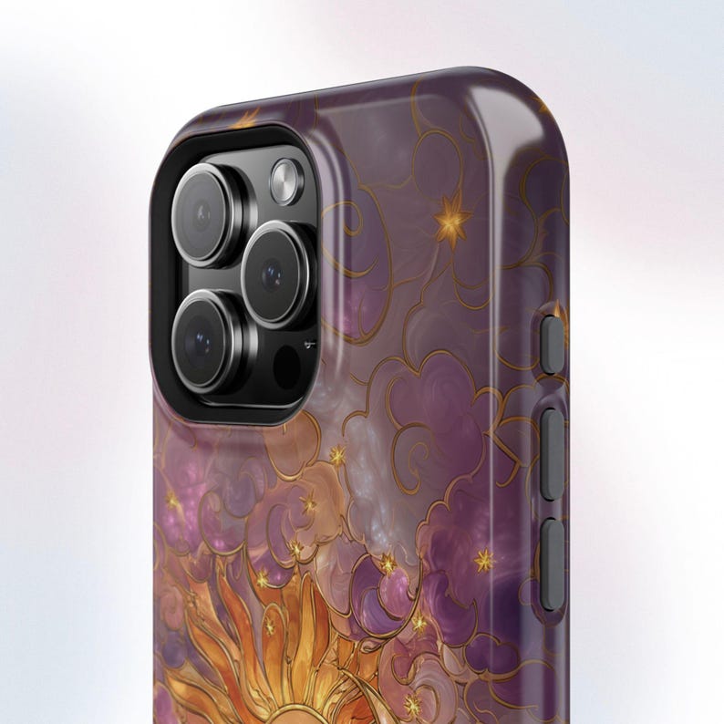 May include: A close-up of a phone case with a celestial design. The case features a vibrant sun, clouds, and stars in shades of gold, orange, purple, and white. The phone's camera lenses are visible.