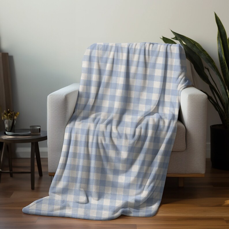 May include: A soft blue and white checkered throw blanket draped over a white armchair. The blanket is made of a plush, fuzzy material and has a subtle sheen.
