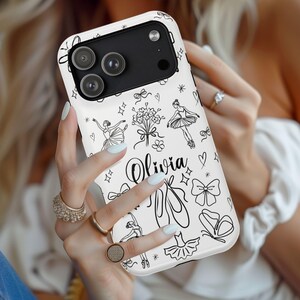 May include: White phone case with a black camera module and a black and white ballet-themed design. The case features illustrations of ballerinas, bows, and ballet shoes, with the name "Olivia" in cursive.