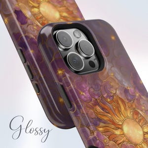May include: Glossy phone case with a celestial design featuring a sun, stars, and clouds in shades of purple, orange, and gold. The case has a black border and a glossy finish. The word "Glossy" is written in cursive.