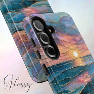 May include: Glossy phone case with a sunset design. The case features a vibrant blend of blue, pink, and gold colors, with a glossy finish. The design resembles a sunset over the ocean. The case has a triple-lens camera cutout.