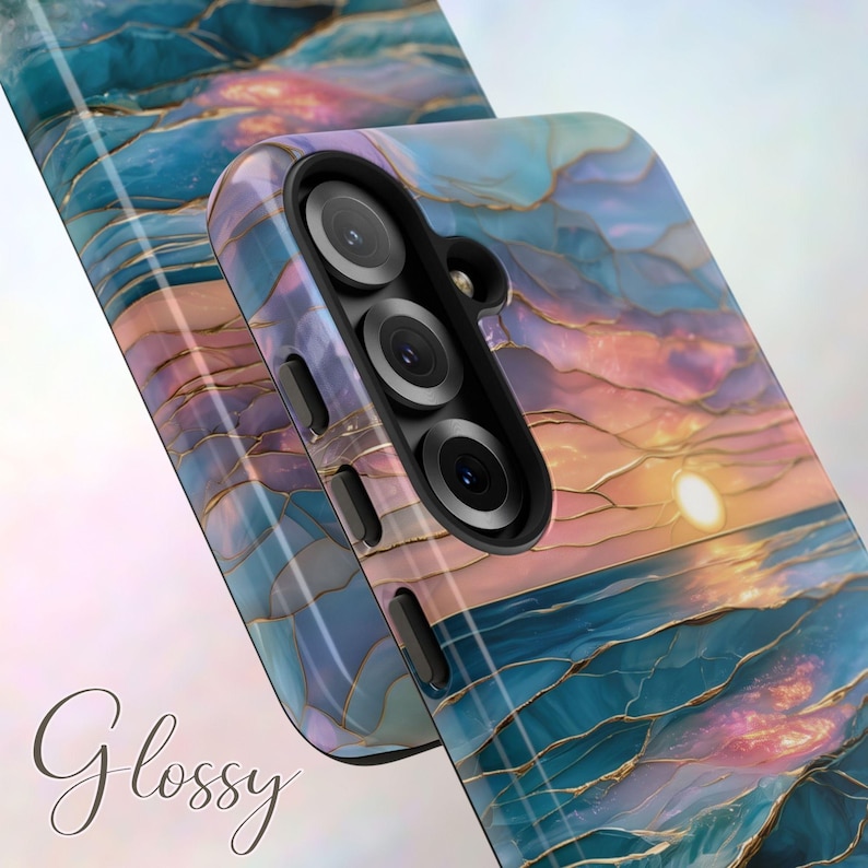 May include: Glossy phone case with a sunset design. The case features a vibrant blend of blue, pink, and gold colors, with a glossy finish. The design resembles a sunset over the ocean. The case has a triple-lens camera cutout.