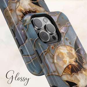 Pu&ograve; includere: Una cover per telefono lucida con un design in stile vetrata che raffigura una grande luna, pipistrelli in volo e piccole stelle. Il motivo utilizza tonalit&agrave; blu, crema e linee dorate. La cover presenta il testo Glossy e tasti neri.