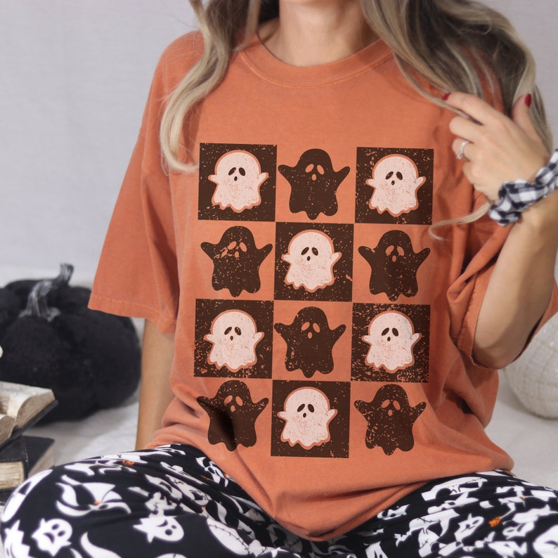 May include: A burnt orange t-shirt with a checkered pattern of white and brown ghosts. The ghosts have a distressed look.