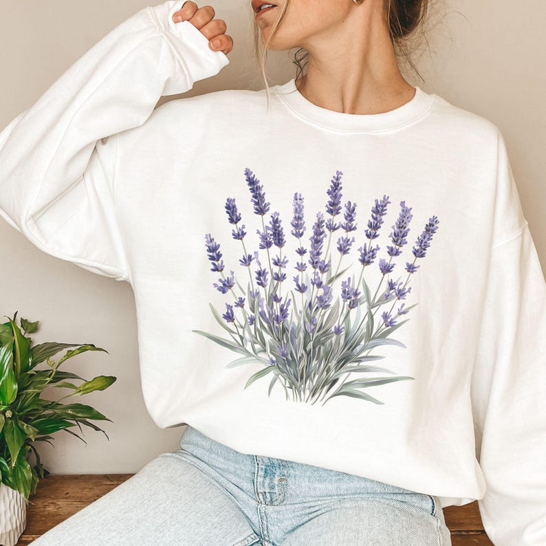 Op de afbeelding: Witte trui met een lavendelbloemendruk. De bloemen zijn paars en groen.
