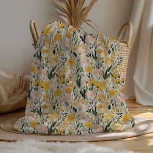 May include: A floral blanket with a pattern of yellow and peach flowers and green leaves. The blanket is folded and placed in a woven basket. The basket is sitting on a round, woven mat.