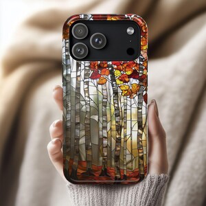 May include: A smartphone case featuring a stained-glass design of a birch tree forest in autumn. The case has a glossy finish and a colorful depiction of red, orange, and yellow leaves. The phone case is held in a person's hand.