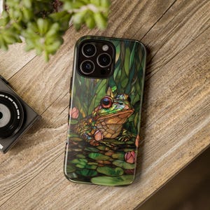 May include: A green, brown, and blue phone case with a stained glass design of a frog sitting on lily pads.