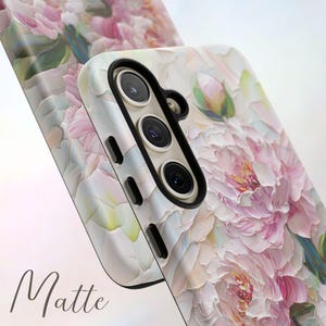 K&ouml;nnte beinhalten: Eine wei&szlig;e Handyh&uuml;lle mit einem Blumendesign aus rosa und wei&szlig;en Pfingstrosen. Die H&uuml;lle hat eine matte Oberfl&auml;che und einen Kameraausschnitt mit drei Objektiven.