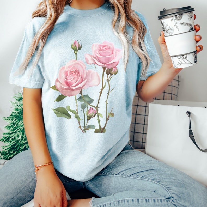 May include: A light blue t-shirt with a floral design featuring pink roses and green leaves.