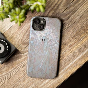 May include: A white iPhone case with a stained glass design featuring a ghost. The case has a clear, iridescent finish and a raised camera bump.