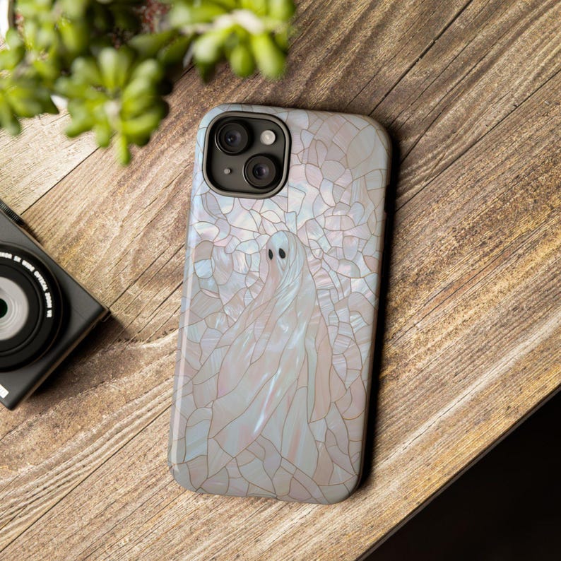May include: A white iPhone case with a stained glass design featuring a ghost. The case has a clear, iridescent finish and a raised camera bump.