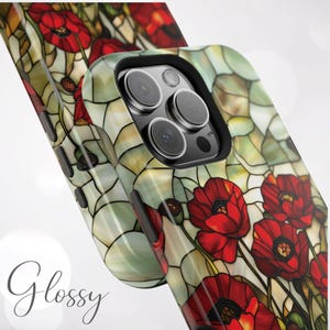 Pu&ograve; includere: Una custodia per telefono con un design a vetri colorati con papaveri rossi su uno sfondo verde e bianco. La custodia ha un rialzo per la fotocamera rialzato con un bordo nero.
