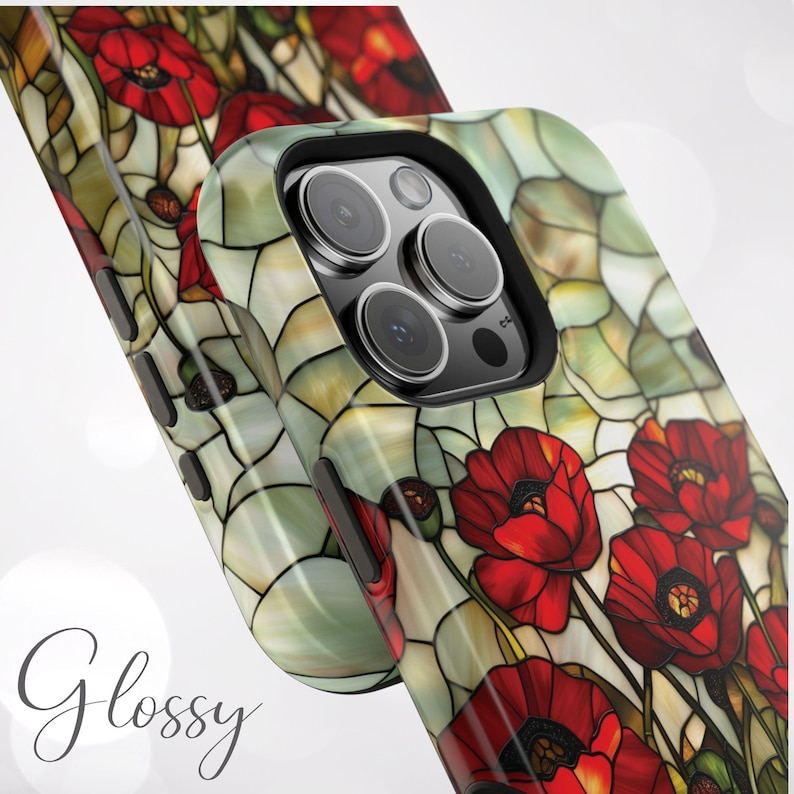 Pu&ograve; includere: Una custodia per telefono con un design a vetri colorati con papaveri rossi su uno sfondo verde e bianco. La custodia ha un rialzo per la fotocamera rialzato con un bordo nero.