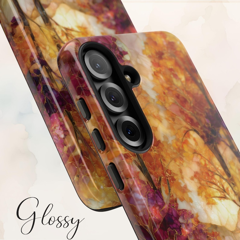 May include: Glossy phone case featuring a vibrant autumn-themed design. The case showcases a blend of warm colors, including orange, yellow, and burgundy, with a glossy finish. The design resembles a watercolor painting of fall foliage. The phone case has a triple-lens camera.