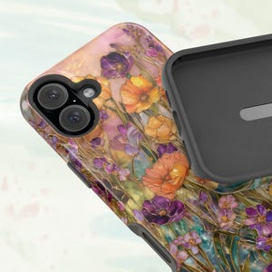 Op de afbeelding: Een telefoonhoesje met een bloemenontwerp in tinten oranje, paars en geel. De hoes heeft een zwarte binnenkant en een uitsparing voor de camera. Het ontwerp doet denken aan een aquarel.