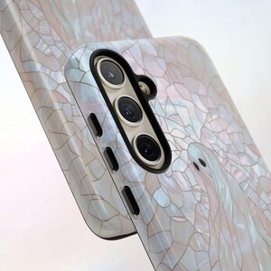 May include: A white phone case with a pearly, mosaic-like design. The case has a raised camera bump with three black lenses.