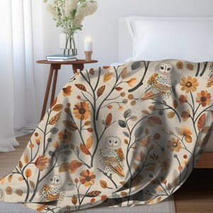 May include: A cream-colored throw blanket with a repeating pattern of owls, leaves, and flowers in shades of brown, orange, and yellow.
