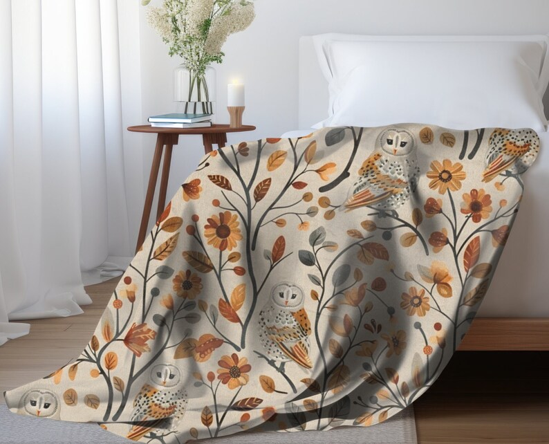 May include: A cream-colored throw blanket with a repeating pattern of owls, leaves, and flowers in shades of brown, orange, and yellow.