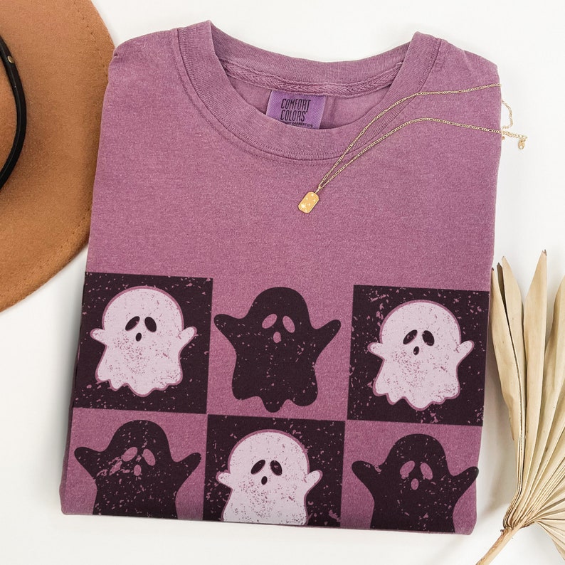 May include: A purple t-shirt with a graphic of six ghosts in a checkered pattern. The ghosts are in black and white and have a distressed look. The shirt has a tag that says "Comfort Colors".