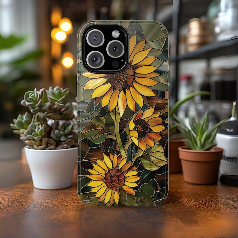 May include: A clear phone case with a stained glass design featuring yellow sunflowers on a green background. The case has a cutout for the phone's camera.