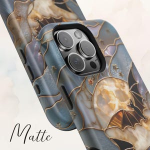 Pu&ograve; includere: Una cover per telefono con finitura opaca e un design in stile vetrata con una luna, stelle e sagome di pipistrelli in tonalit&agrave; blu, oro e crema. La cover presenta un ritaglio nero per la fotocamera. La parola Matte &egrave; scritta in corsivo nero.