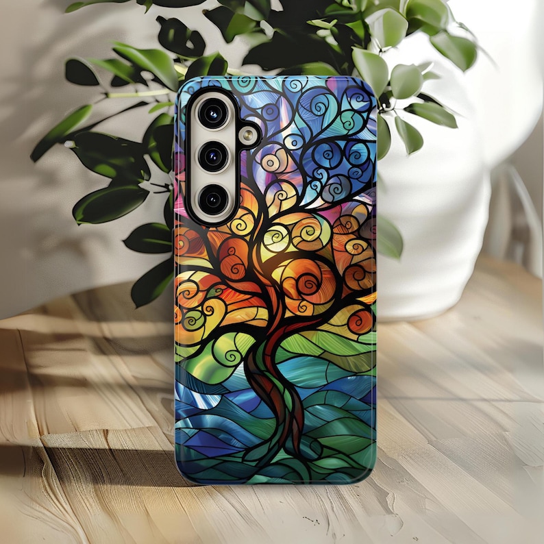 May include: A colorful phone case with a stained glass design of a tree with swirling branches. The case has a black background and a multi-colored tree with blue, green, orange, and yellow accents.
