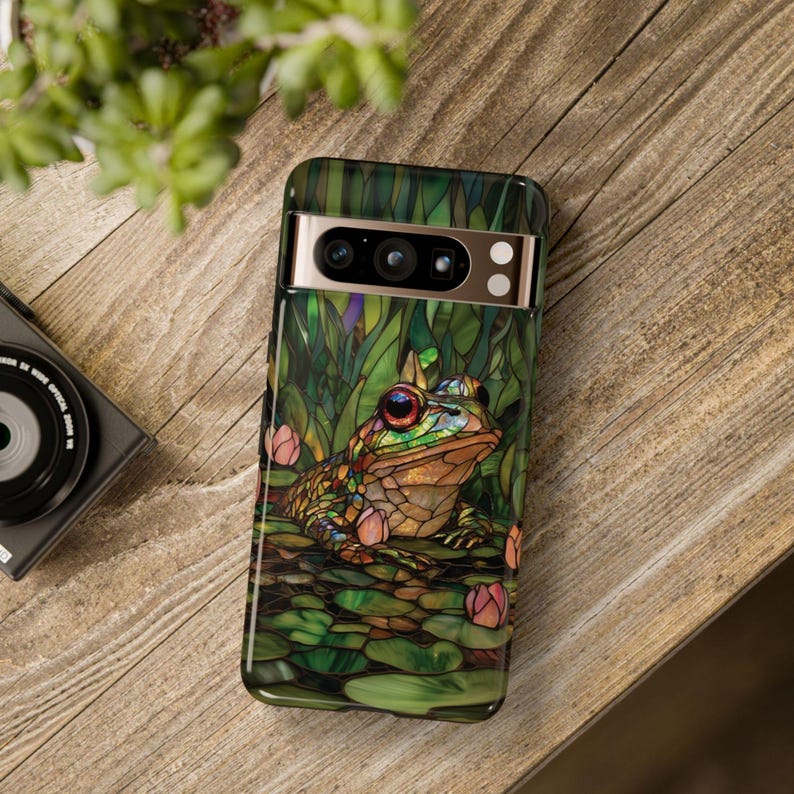 May include: A green, brown, and gold phone case with a stained glass design of a frog sitting on lily pads.