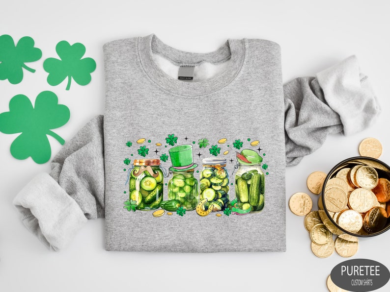 May include: A gray sweatshirt with a print of four jars of pickles. The jars are decorated with shamrocks, a leprechaun hat, and a mustache. The text 'PURETEE CUSTOM SHIRTS' is printed in the bottom right corner.