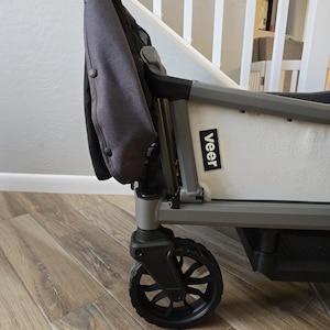 May include: A gray and black Veer wagon with a black wheel and a gray fabric seat. The wagon has a white side panel with the word "Veer" printed on it.