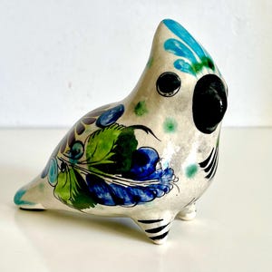 May include: A ceramic bird figurine with a white base, adorned with blue, green, and purple floral patterns. The bird has a black eye and beak, with black stripes on its feet. The figurine is a decorative item.