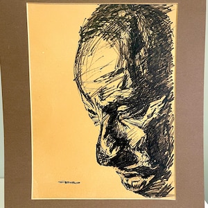 May include: A black and white sketch of a man's face in profile. The artwork is framed in a brown mat and set against a light tan background. The drawing style features bold, expressive lines.
