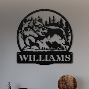 May include: Black metal wall art featuring a wolf howling in a forest scene with mountains and trees. The name "WILLIAMS" is displayed on a banner below the wolf.