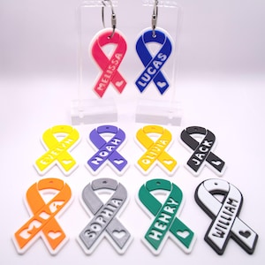 May include: A collection of colorful ribbon-shaped name tags. The tags feature names like Melissa, Lucas, Evelyn, Noah, Olivia, Jack, Mia, Sophia, Henry, and William. Each ribbon has a heart detail.