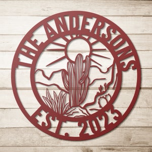 May include: A red metal circle with the text "The Andersons Est. 2023" around the edge. The center of the circle features a desert scene with a cactus, mountains, and a sun.