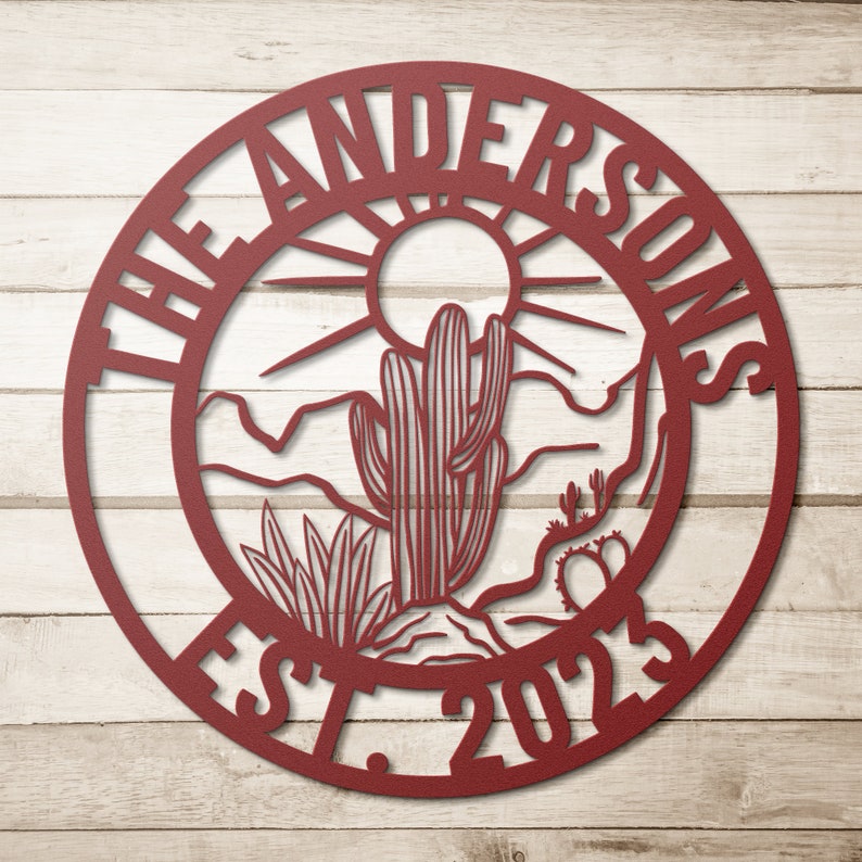 May include: A red metal circle with the text "The Andersons Est. 2023" around the edge. The center of the circle features a desert scene with a cactus, mountains, and a sun.