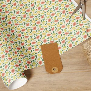 May include: A roll of patterned wrapping paper with a fruit design, featuring red, yellow, and green fruits and leaves. A pair of scissors, a brown tag, and a spool of twine are on a wooden surface.